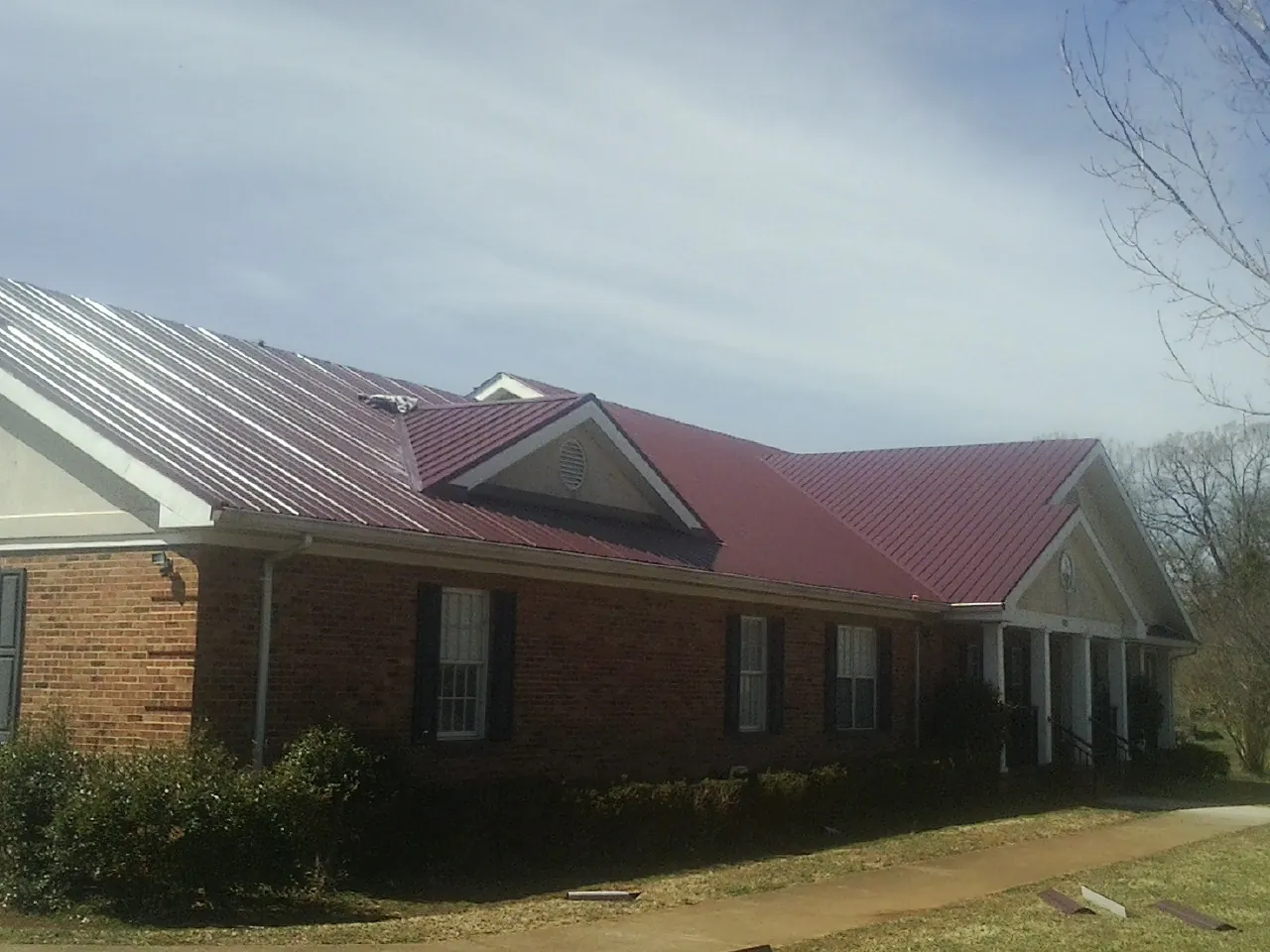 Red metal roof with gabled entries on a long brick building, from a Hail Damage Roof Repair job in Gaffney