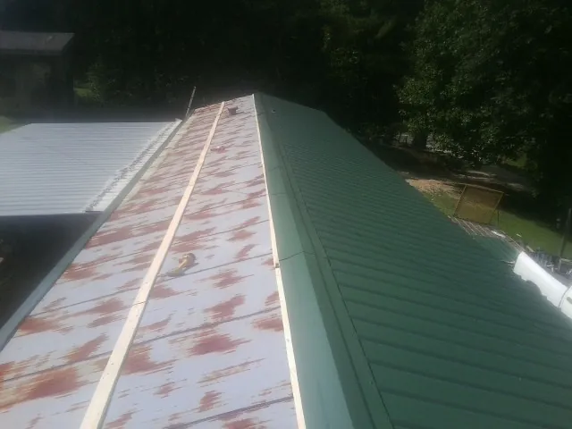 Old rusted panels beside newly installed green metal roofing — Wind Damage Roof Repair by Roofing Brothers in Gaffney