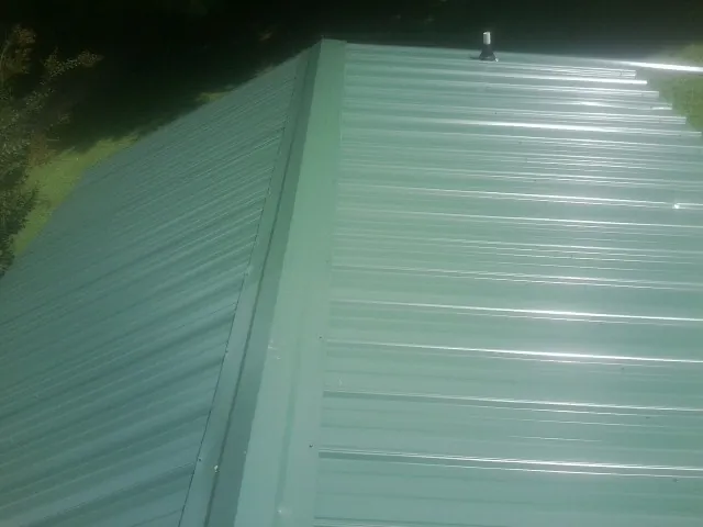 New green metal panels meeting at the ridge of a roof — Flat Roof Repair work by our crew in Gaffney