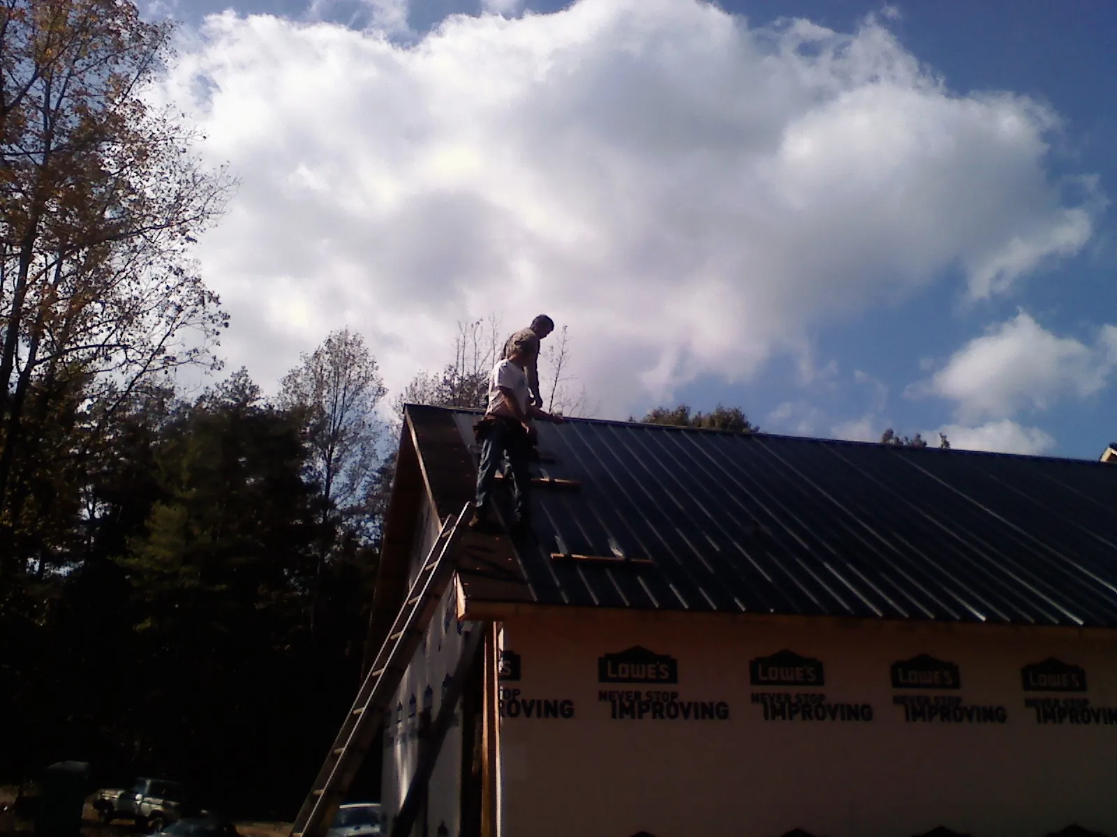 Roofer fastening dark metal panels high against a cloudy sky, from a Roof Inspection job in Gaffney