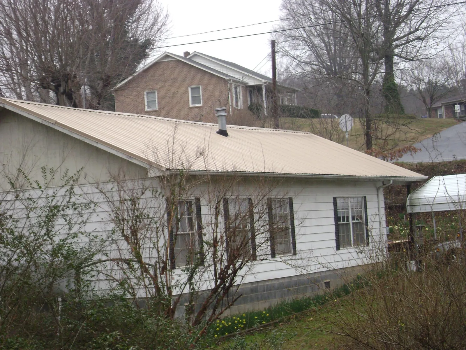 Tan metal roof on a white sided house set into a hillside — Commercial Roofing by Roofing Brothers in Gaffney